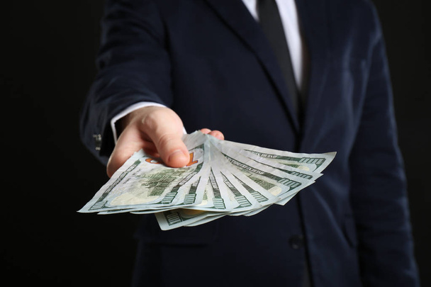 Businessman holding bribe on black background - Foto, Imagen