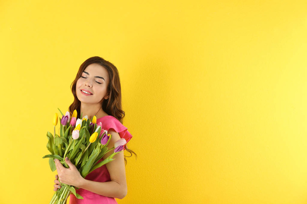 Mooie vrouw met boeket tulpen op kleur achtergrond - Foto, afbeelding