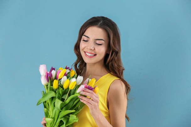 Beautiful woman holding bouquet of tulips on color background - Valokuva, kuva