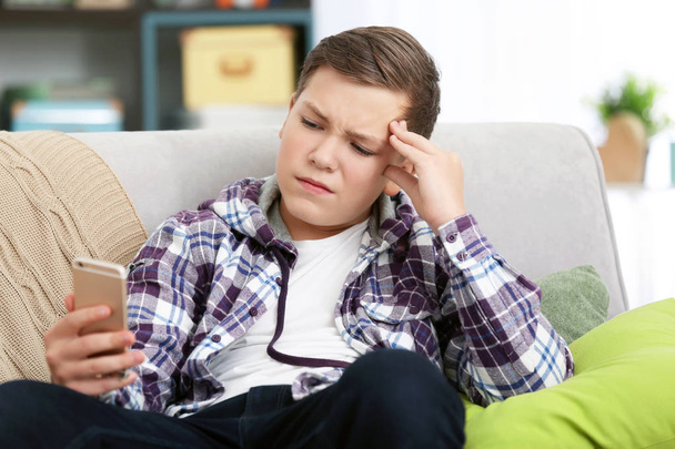 Upset teenage boy with smartphone indoors - Photo, Image