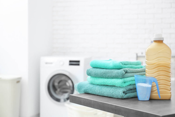 Пачка чистых полотенец и моющее средство на стиральной машине в прачечной
 - Фото, изображение