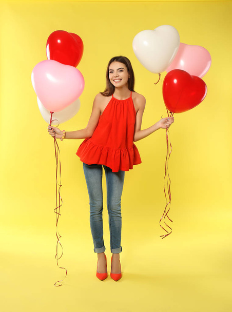 Romantic young woman with heart-shaped balloons for Valentine's Day on color background - Foto, afbeelding