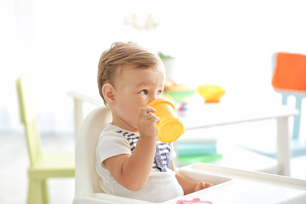 Adorable baby drinking from bottle while sitting in highchair at home - Zdjęcie, obraz