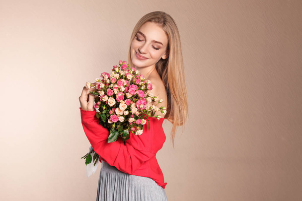 Beautiful young woman with bouquet of roses on color background - Foto, afbeelding