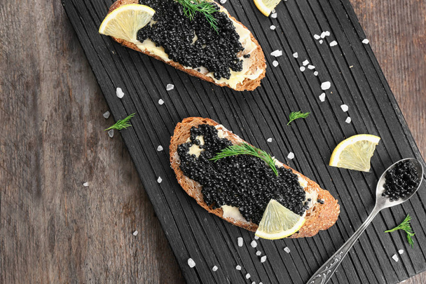 Slices of bread with black caviar and butter on wooden board - Фото, изображение