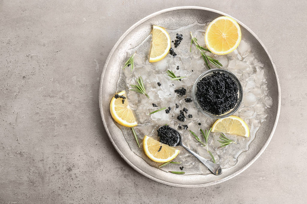 Black caviar served with ice and lemon on metal plate - Foto, imagen