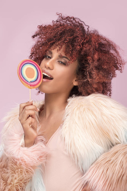 Fashionable afro woman with lollipop on pink background. - 写真・画像