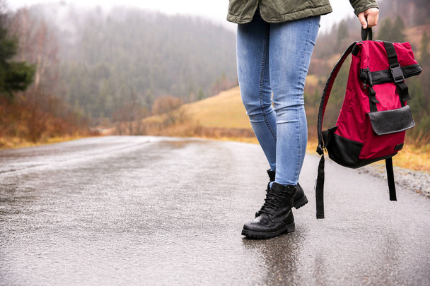 Female tourist with backpack walking along countryside road in the rain - Foto, Imagem