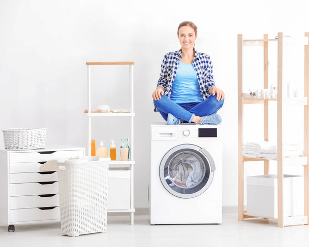 Young woman sitting on washing machine in laundry room - Foto, Bild