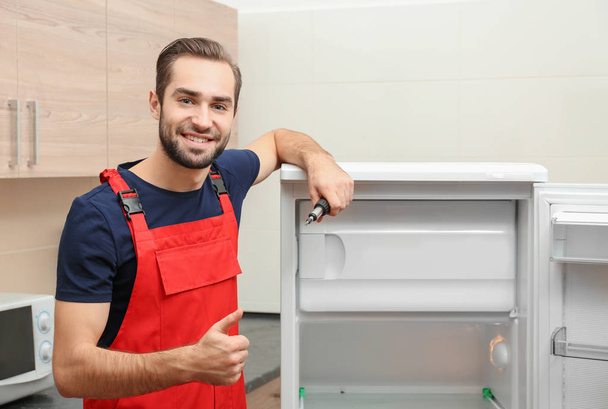 Male technician after successful repair of refrigerator indoors - 写真・画像