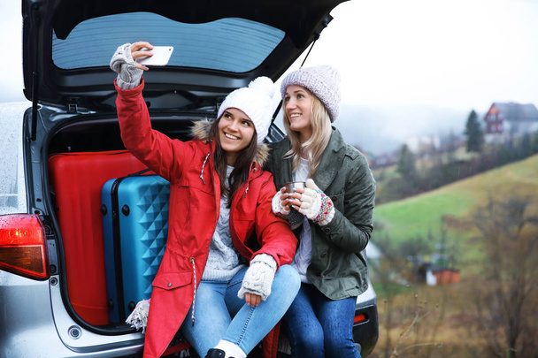 Female tourists taking selfie near car in countryside - Foto, afbeelding