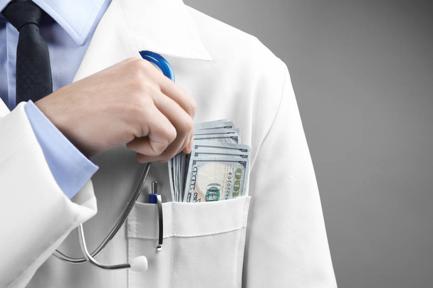 Doctor putting money in pocket on grey background. Corruption concept - Фото, изображение