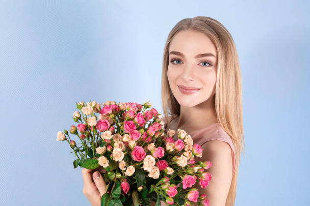 Beautiful young woman with bouquet of roses on color background - Valokuva, kuva