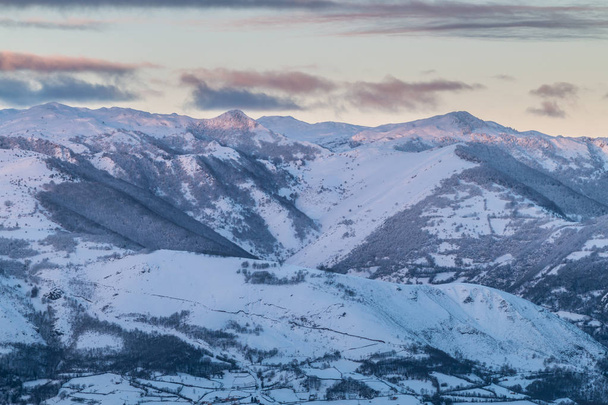 zonsopgang in de bergen van Ubina, tussen het Asturië en León, op een winterdag met veel sneeuw, vroeg in de ochtend te fotograferen de unieke kleuren van de eerste zonnestralen die contrasteren met de sneeuw, de wolken en de berg ... - Foto, afbeelding