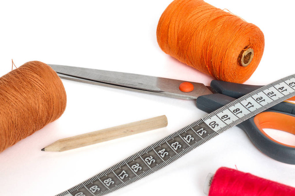 Scissors, a centimeter and a pencil. Spools of thread red, orange and brown. On a white background. - Foto, Imagen