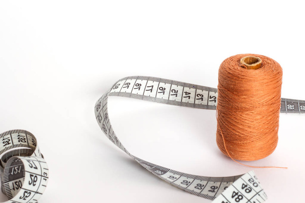Accessories for sewing: thread and centimetre on a white background. Brown bobbin thread. - Fotografie, Obrázek