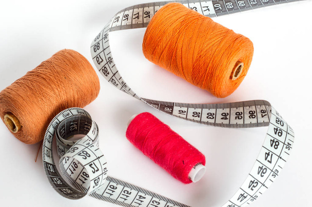 Accesorios para coser: hilo, aguja y centímetro sobre fondo blanco. Hilo de bobina naranja, marrón y rojo
. - Foto, Imagen