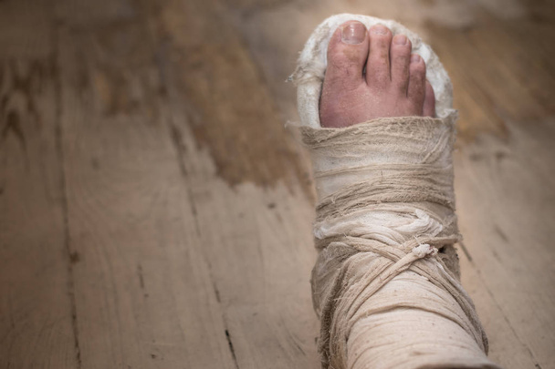 Сломанная нога в штукатурке на потрепанном деревянном полу
 - Фото, изображение