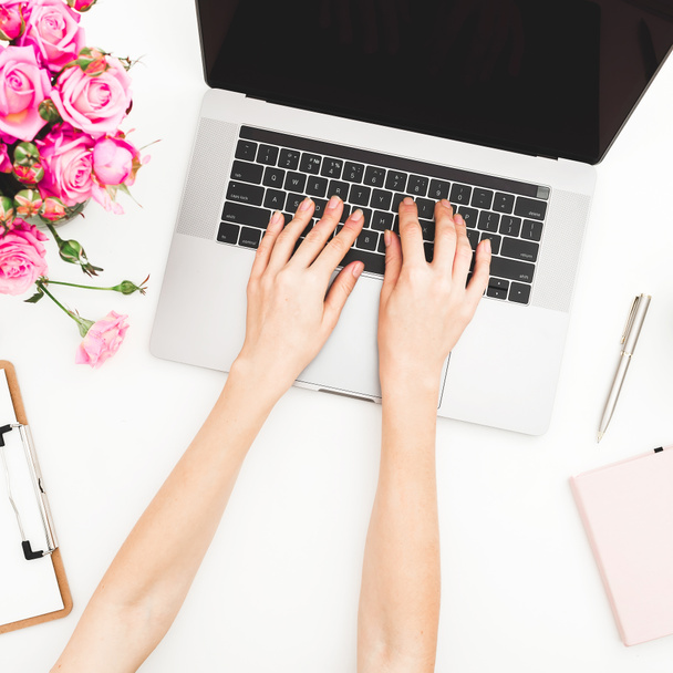 Home office desk. Woman workspace with female hands, laptop, pink roses bouquet, accessories, diary on white. Top view. Flat lay. Girl working on laptop. - 写真・画像