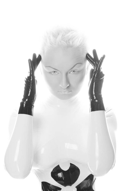 extraña mujer albina alienígena futurista con pelo corto y rubio posando en traje de goma de látex y corsé apretado con guantes negros sobre fondo blanco aislado
 - Foto, Imagen
