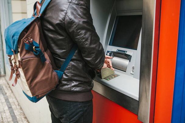 De toerist trekt geld uit de geldautomaat voor verdere reizen. Hiermee kiest u de code met de ene hand en sluit u de knoppen met de andere hand om de informatie te beschermen. - Foto, afbeelding