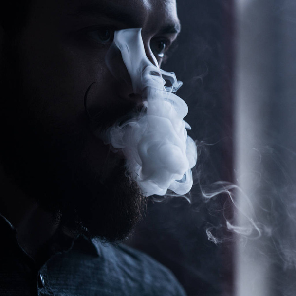 Sakal ve Mustages Vaping elektronik sigara olan adam. Vaper Hipster duman Buharlaştırıcı ve Exhals duman akış. - Fotoğraf, Görsel
