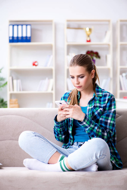 Студентка сидит на диване с мобильным телефоном - Фото, изображение