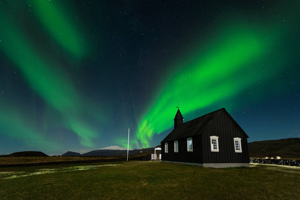 Northern Lights over The Black Church Budir, Islandia. Aurora Boreal en un paisaje nocturno increíble. Destino de viaje con hermosas luces verdes paisaje
. - Foto, imagen