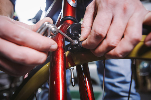 Thema Reparaturfahrräder. Nahaufnahme der Hand eines kaukasischen Mannes mit einem Sechskant-Handwerkzeug zum Einstellen und Anbringen von Felgenbremsen an einem roten Fahrrad - Foto, Bild