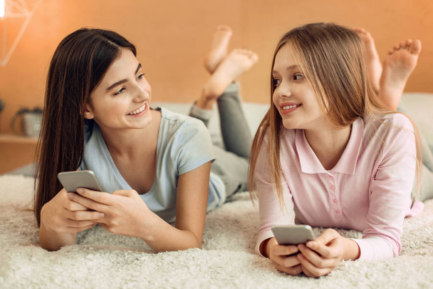 Cheerful girls talking while using their phones - Zdjęcie, obraz