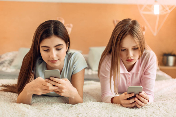 Teenage girls lying on bed and using their phones - Fotoğraf, Görsel