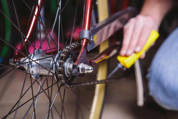 Thema reparatie fietsen. Close-up van een blanke man's hand gebruiken een ketting smeermiddel in een gele lubricator voor llubricator een fietsketting op een rode fiets - Foto, afbeelding