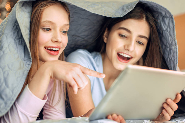Cheerful girls watching video under blanket - Foto, afbeelding