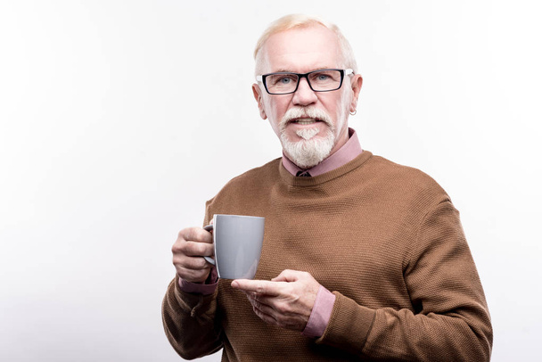 Pleasant elderly man in eyeglasses holding coffee cup - Foto, afbeelding