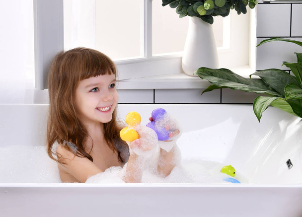  Feliz menina sentada na banheira brincando com brinquedos de pato no banheiro
 - Foto, Imagem