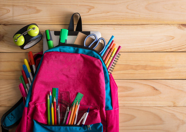 Шкільний рюкзак зі шкільними приладдям та годинником на дерев'яному столі
. - Фото, зображення