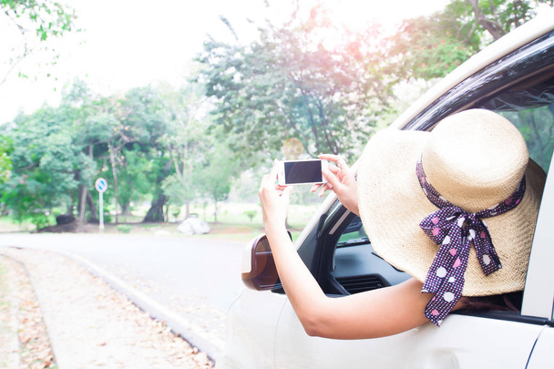 Turystyczny Kobieta w kapeluszu smartfona biorąc zdjęcie z jej samochodu, podróży i szczęśliwe życie - Zdjęcie, obraz