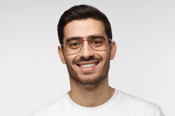 Close up portrait of smiling handsome man in trendy glasses and white t-shirt isolated on light gray background - Valokuva, kuva