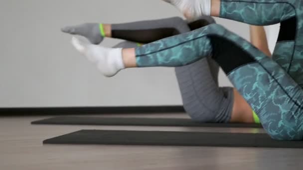 im Fitnessstudio während der Pilates-Übung auf den Gymnastikmatten liegend ziehen zwei Mädchen, die auf dem Rücken liegen, abwechselnd ihre Knie zur Brust und dehnen die Muskeln der Oberschenkel. synchrone Ausführung der - Filmmaterial, Video