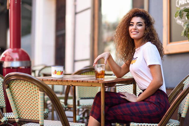 Arab girl in casual clothes drinking a soda in an outdoors bar - Photo, Image