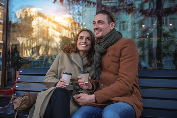 Cheerful man and woman drinking beverage on bench - Foto, afbeelding