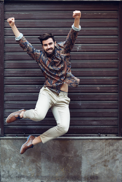 Jovem barbudo homem pulando no fundo urbano com os braços abertos wea
 - Foto, Imagem