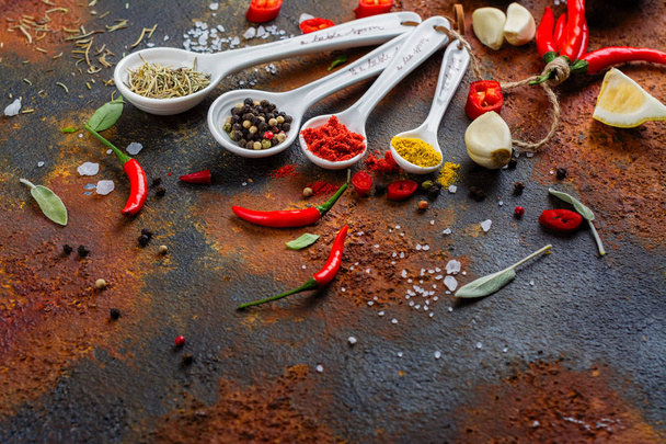 Dry herbs and spices in measuring spoons on white stone kitchen table - Foto, afbeelding