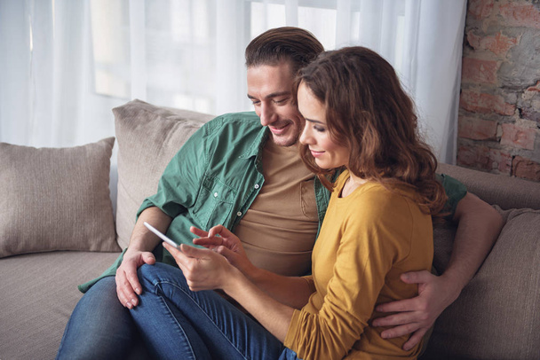 Happy lovers entertaining with gadget in living room - Foto, imagen