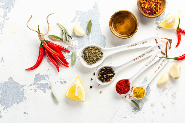 Dry herbs and spices in measuring spoons on white stone kitchen table - Fotografie, Obrázek