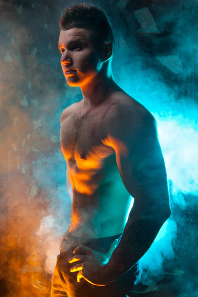 masculine young muscular male standing with naked torso in the smoke on a black background in Studio - Foto, imagen