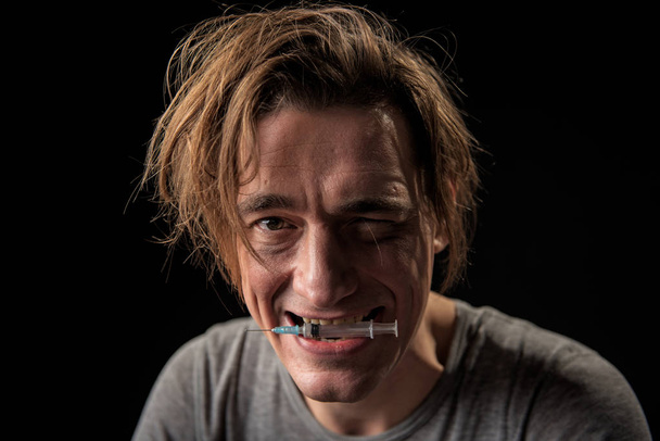 Glad stoned freak holding used syringe with teeth - Foto, afbeelding