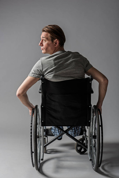 Melancholy disabled young man taking seat in special armchair - Photo, Image