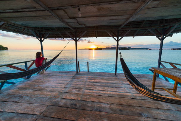 Îles Togean Sunrise, Îles Togiennes destination de voyage, Sulawesi, Indonésie. Femme regardant la vue sur l'hamac, eau turquoise transparente avec des îlots dispersés
. - Photo, image