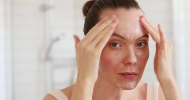 Mujer aplicando crema hidratante en su cara en el espejo
 - Imágenes, Vídeo